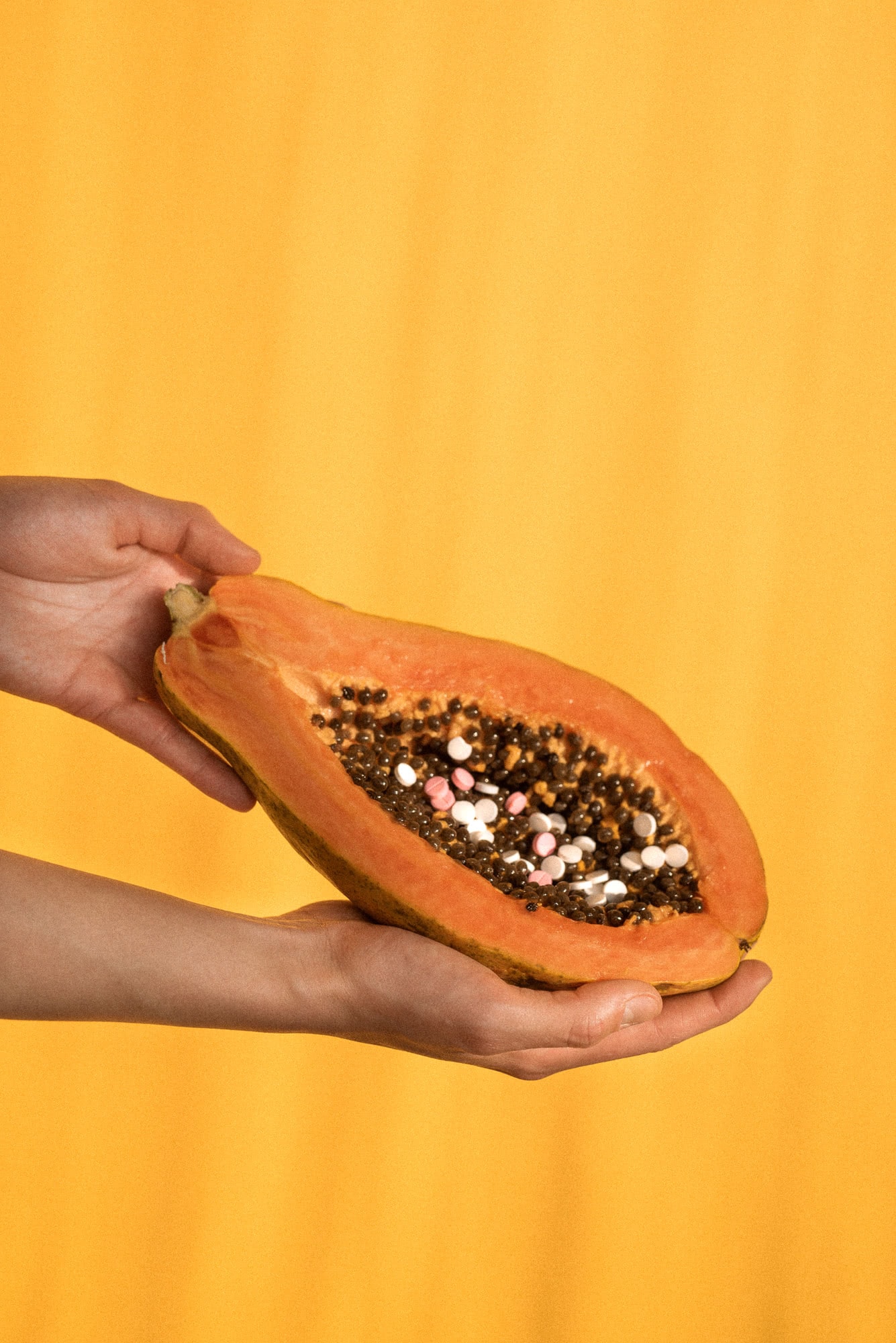 Kolorowe tabletki przeznaczone do aborcji farmakologicznej ułożone na owocu papai, który leży w rękach dziewczyny.