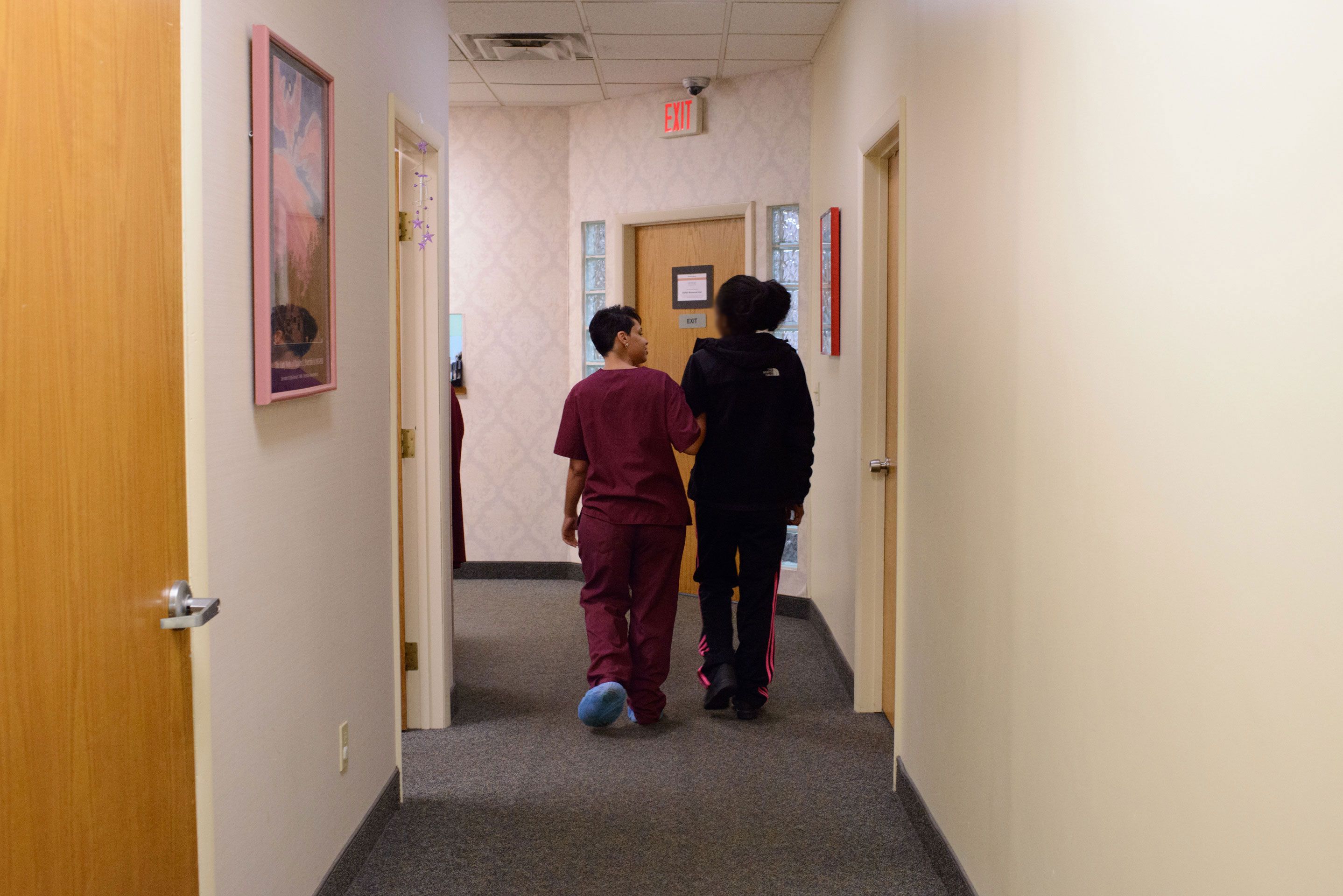 Pielęgniarka odprowadza pacjentkę kliniki po przeprowadzonej aborcji korytarzem trzymając się pod rękę.