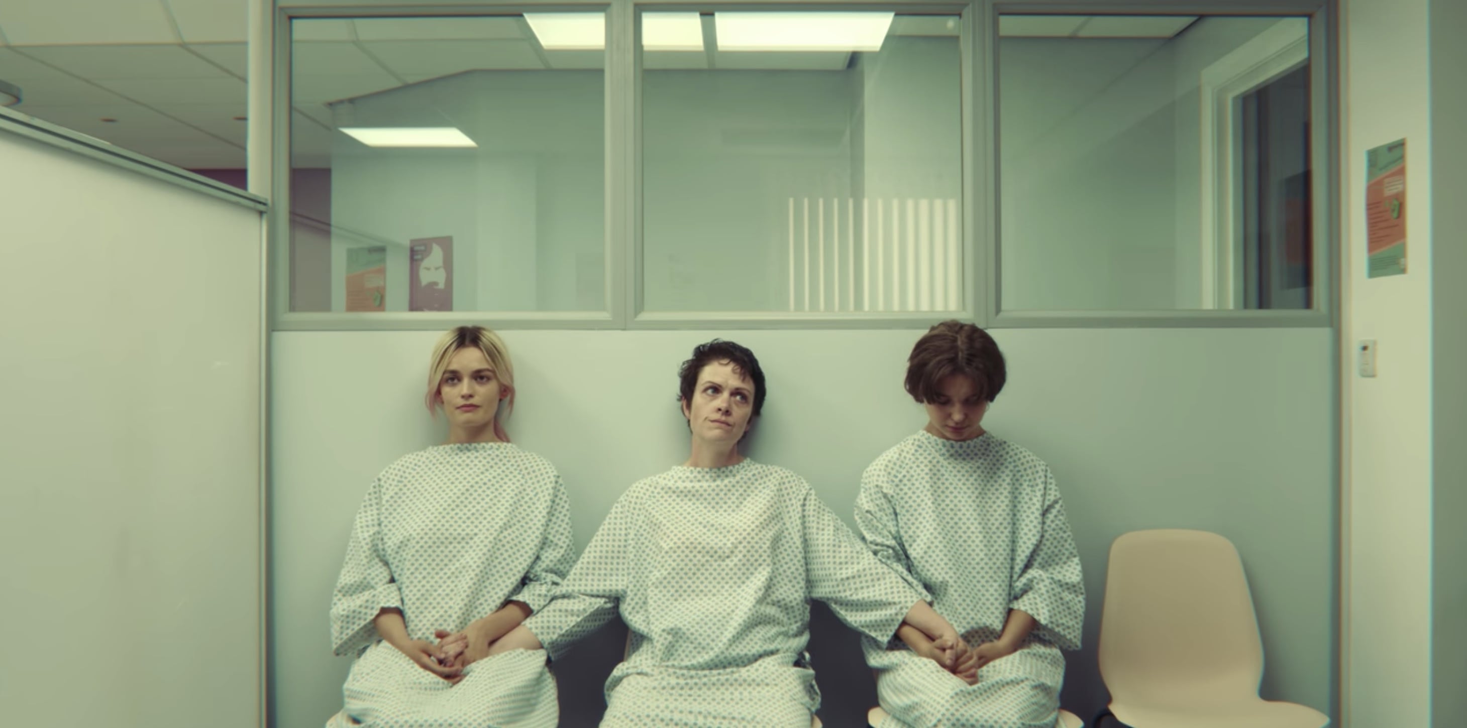 Scena z serialu Netflixa Sex Education - trzy kobiety w białych fartuchach medycznych siedzą w klinice aborcyjnej trzymając się za ręce. 